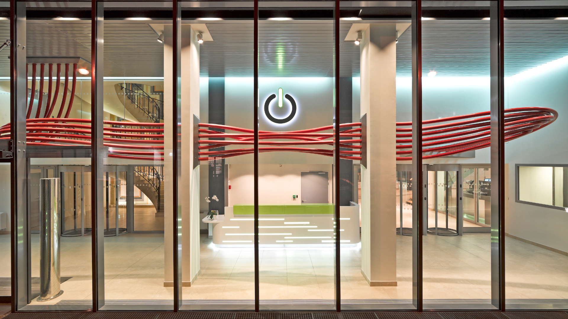 Glass-front reception area with red sculptural cables and a large illuminated power symbol on the back wall behind the desk from the lobby view.