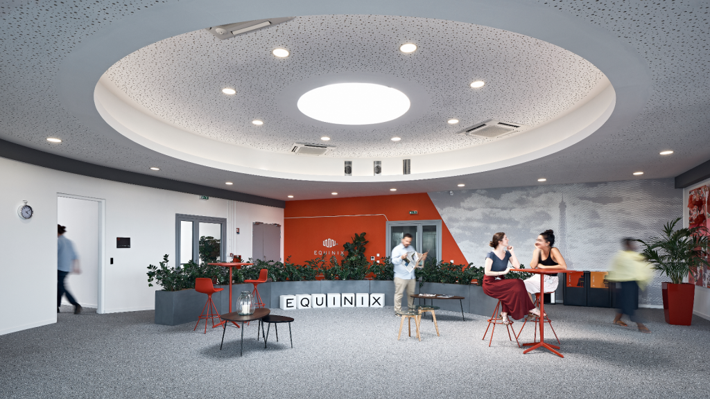 Open lobby with circular illuminated ceiling, orange wall, and people sitting at red high tables near planters and EQUNIX blocks on the floor.